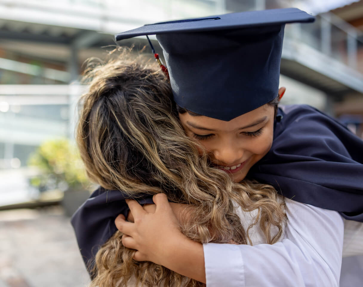 Teenager wearing a graduation cap hugging a child outdoors, representing education milestones and future planning.