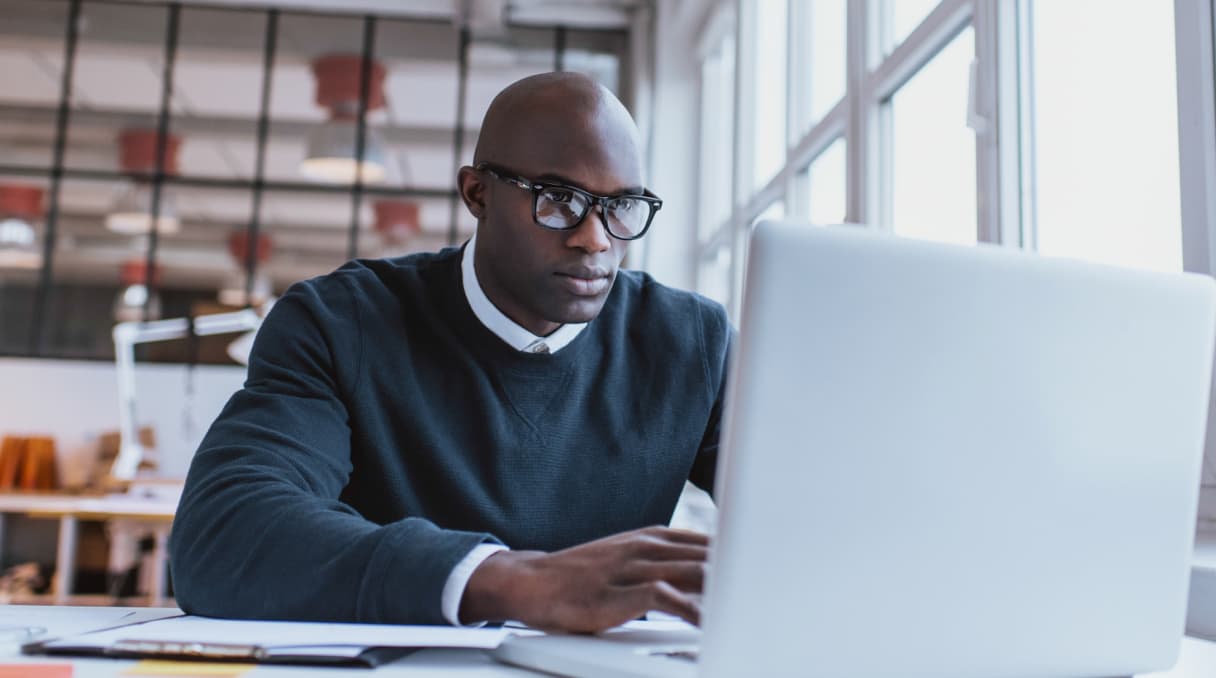 Man in glasses sits in front of a laptop.