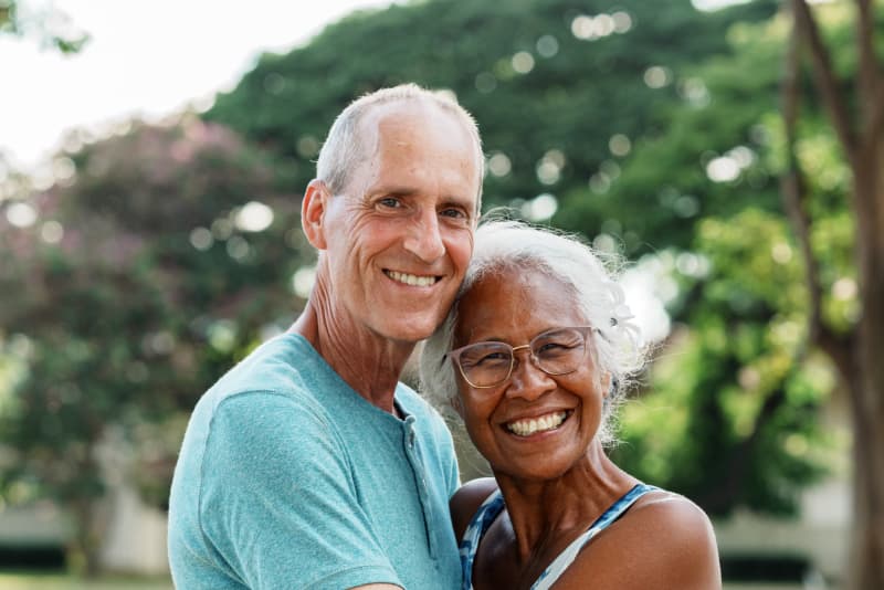 An older couple smiling and embracing outdoors.