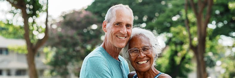 An older couple smiling and embracing outdoors.