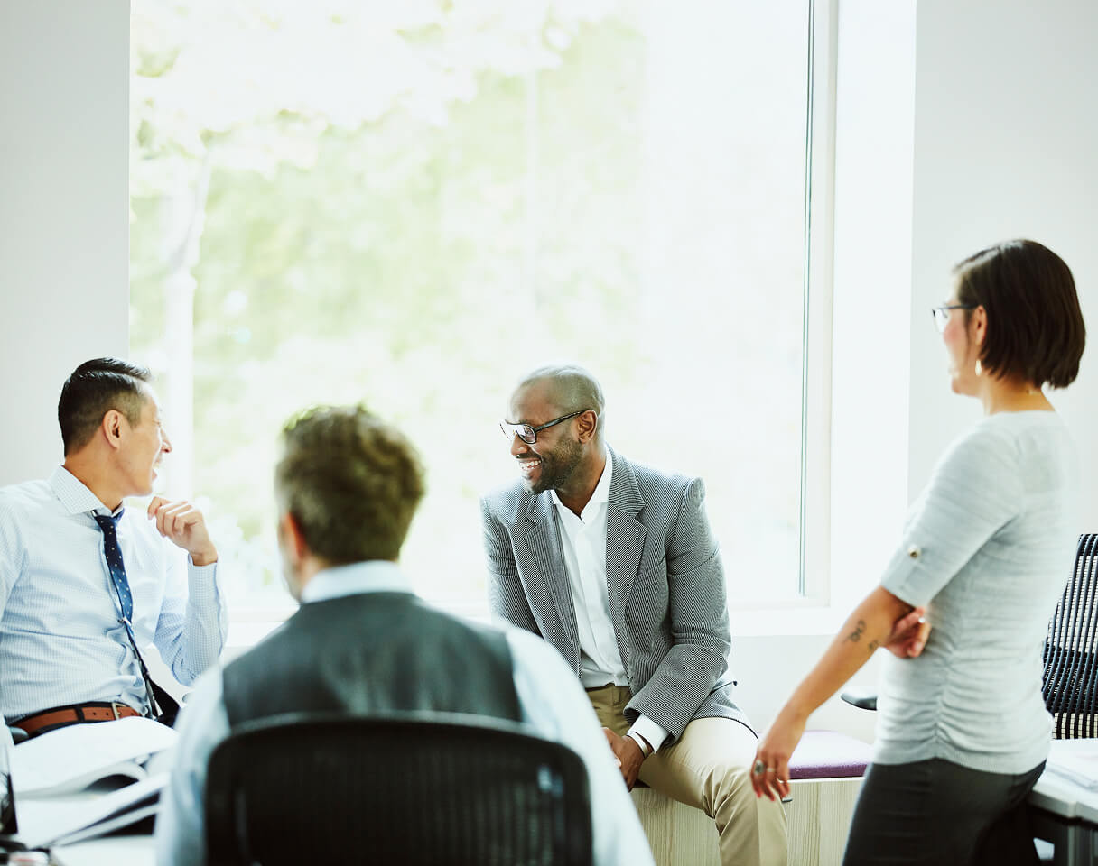 Four Consultants talk and laugh around a conference table in a bright office