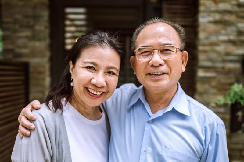 A middle-aged couple smiling and embracing in front of a stone building exterior