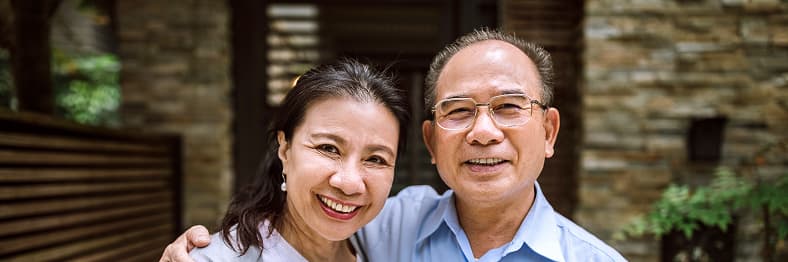 A middle-aged couple smiling and embracing in front of a stone building exterior.