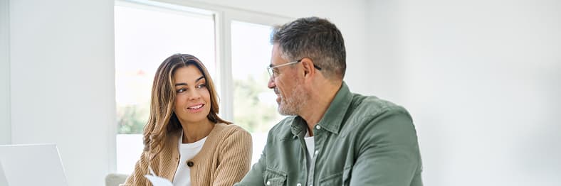 A man and woman sitting at a table indoors, engaged in conversation.