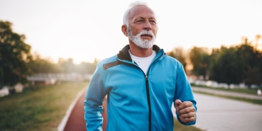 A man with grey hair and wearing a bright blue windbreaker jogs along the side of the road.