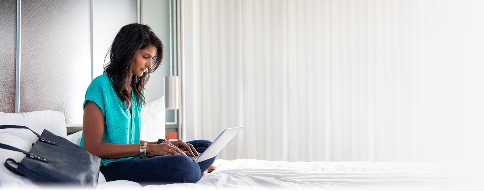 Woman sitting on bed working on laptop