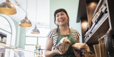 Small business woman standing behind counter holding baked goods and smiling