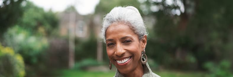 A woman with short gray hair smiling while standing outside in a garden.