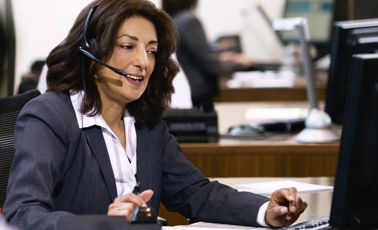 Female customer service agent in a suit, wearing a headset, sitting at her desk, looking at a computer screen