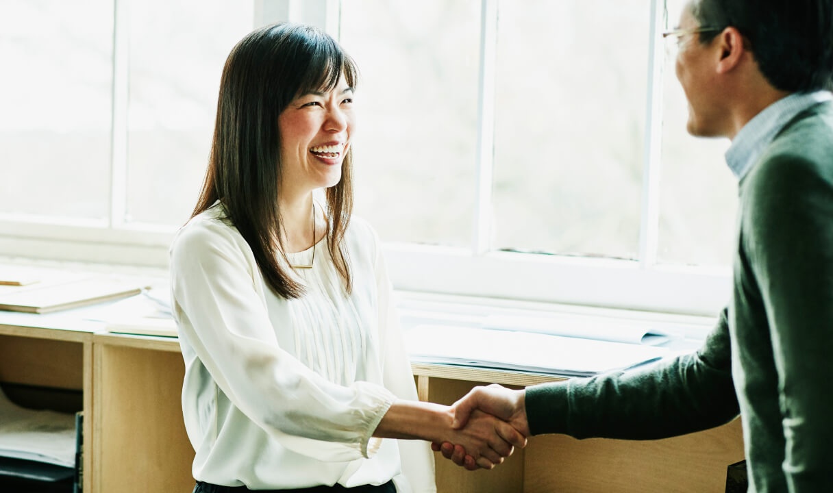 A Schwab Financial Consultant shakes hands with a smiling client in a bright office.